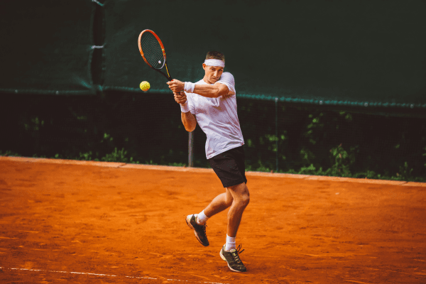 Tennis player hitting a backhand on a clay court