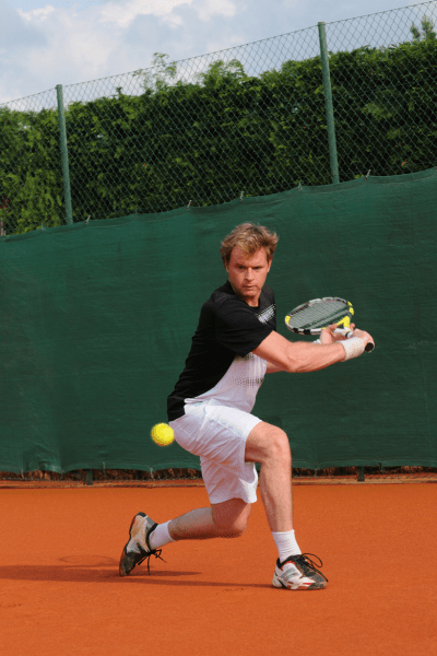 Tennis player striking a backhand on a clay court